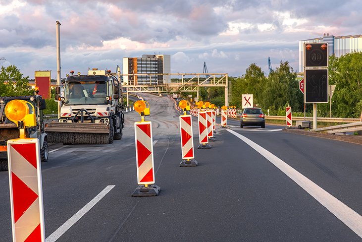 Autobahnbaustelle mit Fahrbahnbegrenzungen und einem Straßenbaufahrzeug auf der linken Spur