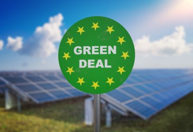 Auf einem grünen runden Schild steht: Green Deal; im Hintergrund sind Solarpanele zu sehen Auf einem grünen runden Schild steht: Green Deal; im Hintergrund sind Solarpanele zu sehen