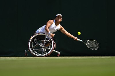 Tennisspielerin von der Seite im Rollstuhl, streckt sich, um Ball mit dem Schläger zu erreichen, Lippen aufeinandergepresst.