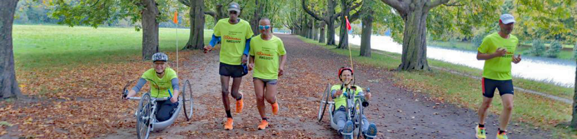 Sportler und Sportlerinnen, mit und ohne Behinderungen laufen durch einen Park.